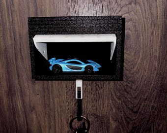 May include: A black wall-mounted key holder with a small display shelf. A light blue toy car is displayed inside the shelf. A key ring with keys hangs below the shelf. The key holder is mounted on a wooden wall.