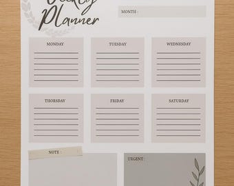 Op de afbeelding: Een witte weekplanner met een minimalistisch ontwerp. De planner bevat secties voor elke dag van de week, samen met ruimtes voor notities en dringende items. De tekst "Weekly Planner" wordt weergegeven in een stijlvol lettertype.