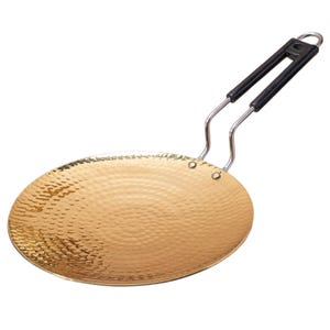 Pode incluir: Uma frigideira plana e redonda de metal dourado com uma textura martelada na superfície. A frigideira possui um cabo longo de metal prateado com duas pegas de plástico preto na extremidade, fixadas firmemente com dois rebites visíveis.
