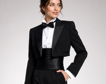 May include: A black tuxedo suit featuring a cropped jacket with satin lapels, a white button-down shirt, a black bow tie, and a wide black satin cummerbund. The ensemble includes tailored black trousers with a straight-leg cut and black heels.