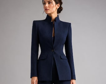 May include: A dark navy blue suit consisting of a structured blazer with a high mandarin collar, a single front button, and long sleeves, paired with matching straight-leg trousers. A small black handbag and black pointed-toe heels are included.