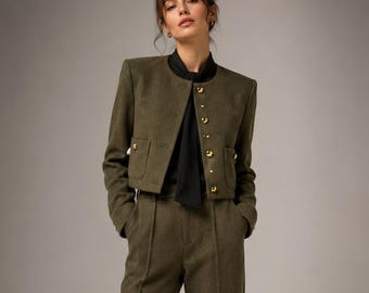 Puede incluir: Una chaqueta corta de color verde oliva con botones dorados y pantalones a juego de cintura alta y pernera ancha. La chaqueta presenta un cuello redondo y dos bolsillos delanteros. Debajo se lleva una camisa negra con detalle de lazo.
