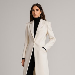 Könnte beinhalten: Ein langer, cremefarbener Mantel mit taillierter Silhouette. Der Mantel hat einen Ein-Knopf-Verschluss und ein fallendes Revers. Das Model trägt einen schwarzen Rollkragenpullover und eine schwarze Hose. Die Mantellänge reicht bis zu den Knöcheln.
