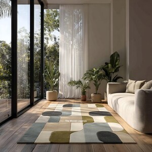 May include: A modern area rug with an abstract geometric design in shades of beige, green, gray, and blue. The rug is rectangular and placed on a hardwood floor. The text "The Woven Legacy" is visible on the rug.