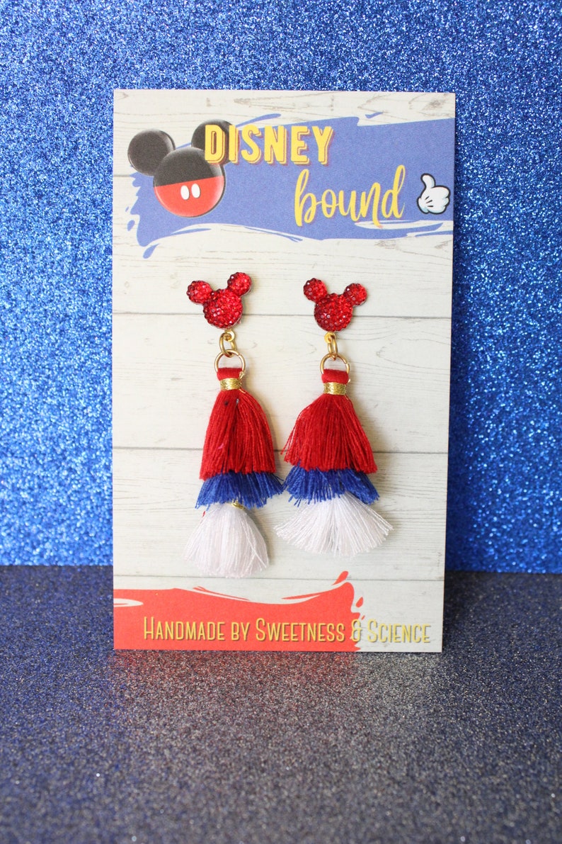 May include: Red, white, and blue tassel earrings with a red glitter Mickey Mouse head charm. The earrings are displayed on a card that says "DISNEY bound" and "HANDMADE BY SWEETNESS & SCIENCE".
