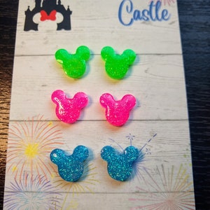May include: A set of six glittery Mickey Mouse ear earrings in green, pink and blue. The earrings are displayed on a card with the text "Race You to the Castle" and "Handmade by Sweetness & Science".