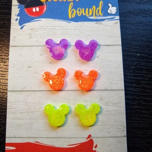 May include: Six pairs of glitter Mickey Mouse ears in purple, orange, and yellow. The ears are displayed on a white card with the text "DISNEY bound" and "HANDMADE BY SWEETNESS & SCIENCE".