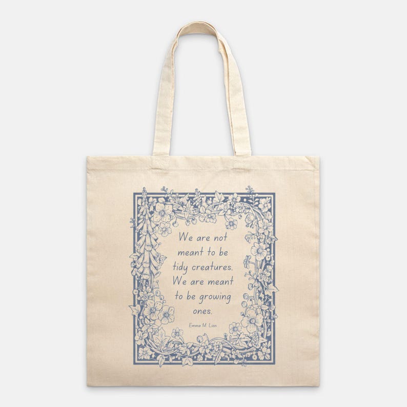 Puede incluir: Bolso tote de color crema con un dise&ntilde;o floral azul y la cita: "No estamos destinados a ser criaturas ordenadas. Estamos destinados a crecer". La bolsa tiene dos asas y est&aacute; hecha de una tela resistente.