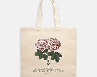 Puede incluir: Bolso tote de color crema con un diseño floral de flores rojas y blancas y hojas verdes. El bolso tiene la cita "I am, in fact, making a go of it. THAT IS MY GREAT TRIUMPH" de Emma M. Lion.