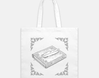 Puede incluir: Bolso tote blanco con una ilustración en blanco y negro de un libro antiguo y una pluma. El diseño está enmarcado por elementos decorativos en las esquinas. Un accesorio práctico y elegante.