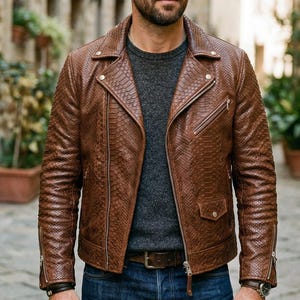 May include: A brown leather jacket with a textured snakeskin pattern. The jacket has a classic biker style with a notched collar, asymmetrical zipper, and multiple pockets. The model is wearing a gray sweater and blue jeans.