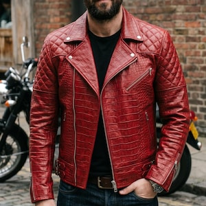 Pode incluir: Casaco de motociclista em couro vermelho com um padrão acolchoado nos ombros e braços. O casaco tem fecho de correr, vários bolsos e ferragens prateadas. O modelo veste uma camisa preta e calças de ganga azuis.