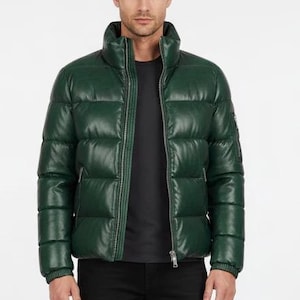 May include: A dark green puffer jacket with a high collar and a front zipper. The jacket has a quilted design and is worn with a black shirt and black pants. The jacket is a stylish outerwear piece.