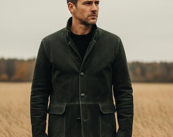 May include: A dark green suede jacket with two front pockets and button closures. The jacket is paired with black pants and brown shoes. The person is standing in a field of tall, dry grass under an overcast sky.
