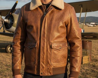 May include: A brown leather jacket with a cream-colored shearling collar. The jacket has two front pockets, a zipper closure, and ribbed cuffs and hem. The jacket is worn over a black shirt. The background includes an airplane.