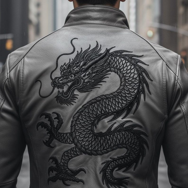 K&ouml;nnte beinhalten: Graue Lederjacke mit einem detaillierten schwarzen Drachen auf dem R&uuml;cken. Der Drache ist aufwendig gestickt, mit Schuppen und feinen Details. Die Jacke hat einen klassischen Kragen und eine taillierte Passform. Stilvolle Oberbekleidung.