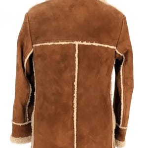 May include: A brown suede jacket with a cream-colored shearling lining and trim. The jacket features a classic design with a notched collar, long sleeves, and a button-up front. The back of the jacket is visible, showcasing the seams and the texture of the suede.