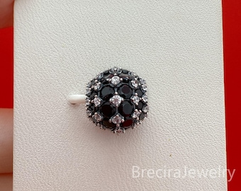 May include: A round, black and silver bead with a cluster of small, clear gemstones. The bead is set against a white background and is held by a small white post. The bead is likely part of a jewelry item, such as a charm or earring.