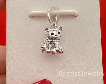 May include: A silver lion cub charm, sitting with detailed paws and a collar. The charm is attached to a silver loop. The background is a white card with the text "BreciraJewelry".