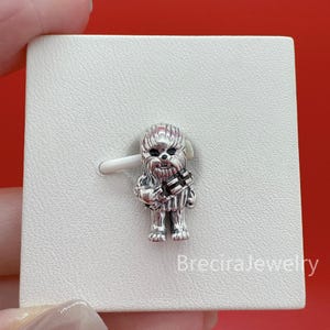 Op de afbeelding: Een zilveren bedel in de vorm van het Star Wars-personage Chewbacca, met gedetailleerde vachttextuur en een donkere bandelier over de borst. De bedel is bevestigd op een witte displaykaart met de tekst BreciraJewelry in de onderste hoek.