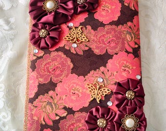 May include: A burgundy fabric covered journal with a floral pattern and gold accents. The journal is decorated with burgundy fabric rosettes and gold butterflies.