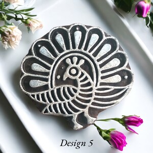 Puede incluir: Un sello de impresión de madera con un diseño detallado de un pavo real con sus plumas de cola extendidas. El sello es negro y blanco y tiene un acabado plateado metálico. El texto "Design 5" está impreso debajo del sello.