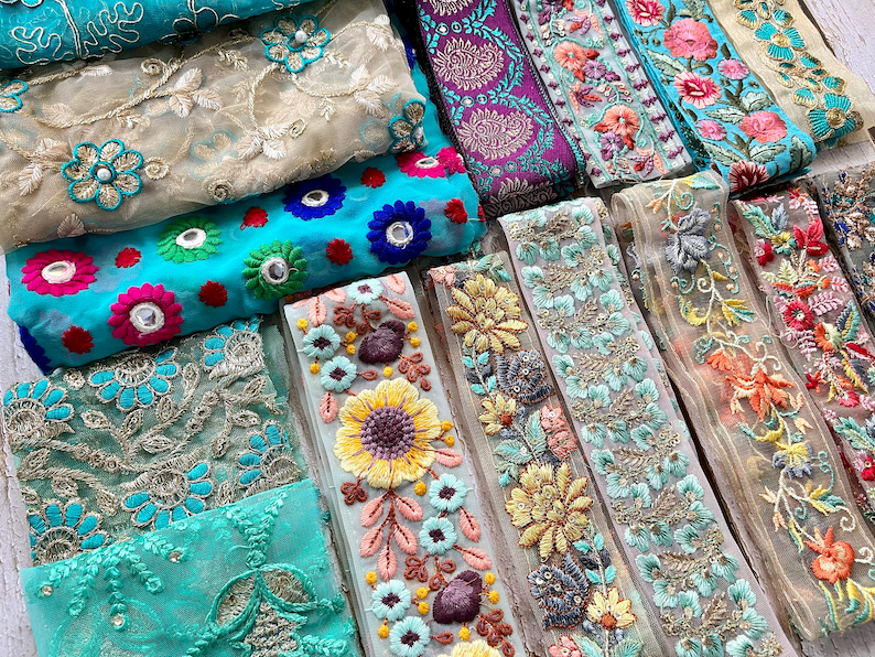 May include: Assortment of colorful embroidered trim with floral and geometric patterns. The trim is made of sheer fabric with a variety of colors, including turquoise, gold, pink, and orange.