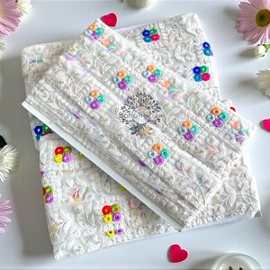 Op de afbeelding: Wit geborduurde stof met kleurrijke bloemaccenten. De stof heeft ingewikkelde patronen en is versierd met kleine, levendige bloemclusters in tinten roze, blauw, geel en paars. Het ontwerp bevat de tekst "BohoTree.com".