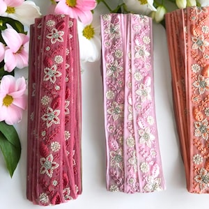 Könnte beinhalten: Drei Rollen rosa, hellrosa und pfirsichfarbener Besatz mit silberner Blumen Stickerei. Der Besatz ist aus einem durchsichtigen Stoff gefertigt und perfekt, um jedem Projekt einen Hauch von Eleganz zu verleihen.