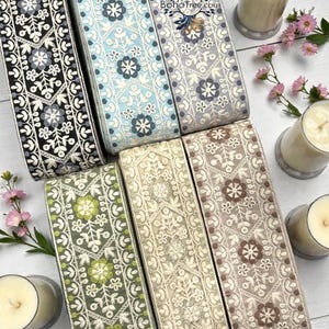 May include: A collection of embroidered ribbons in various colors, including black, blue, green, and beige. Each ribbon features a floral pattern and is displayed alongside lit candles and pink flowers. The website "BohoTree.com" is visible on one of the ribbons.