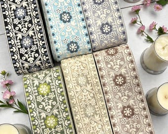 May include: A collection of embroidered ribbons in various colors, including black, blue, green, and beige. Each ribbon features a floral pattern and is displayed alongside lit candles and pink flowers. The website "BohoTree.com" is visible on one of the ribbons.