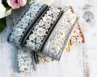 Puede incluir: Surtido de cinco cintas de adorno bordadas con diseños florales blancos sobre fondos de colores diferentes. Las cintas son azul verdoso, negro, blanco, azul claro y marrón.