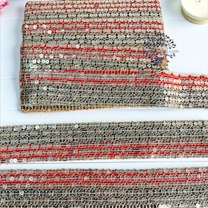 Könnte beinhalten: Eine Rolle dekorativer Borte mit silbernen Pailletten, roten Streifen und goldenen Kanten. Zwei Längen der Borte sind darunter ausgelegt. Die Borte eignet sich zum Verschönern von Kleidung, Accessoires oder Heimdekorationsprojekten.