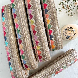 Può includere: Diversi rotoli di passamaneria decorativa con sfondo beige e motivi geometrici colorati. La passamaneria presenta un design a zig-zag con paillettes e una varietà di colori, tra cui rosa, blu, verde e arancione. Adatto per cucito o artigianato.
