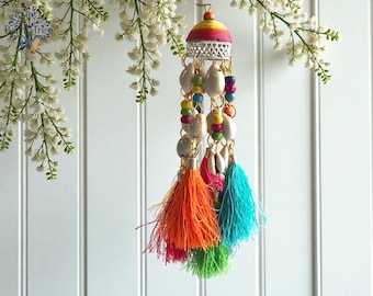 May include: A colorful hanging ornament with a rainbow-striped top, silver filigree, seashells, and beaded accents. The ornament features vibrant orange, pink, green, and turquoise tassels. Decorative item for home decor.