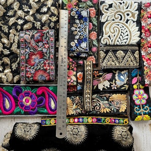 May include: Assortment of colorful embroidered trim with floral and paisley patterns. The trim is on a black background and includes gold and silver accents. A ruler is included for scale.