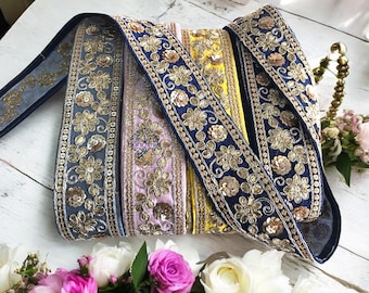 May include: Four different trims of gold and blue embroidered fabric with sequins. The trims are arranged in a row on a white surface.