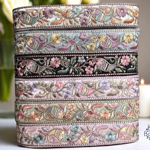 May include: A stack of embroidered ribbons in various colors. Each ribbon features a floral and paisley design with shades of pink, green, blue, and gold. The ribbons are stacked neatly, showcasing the intricate details of the embroidery.