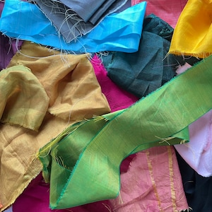 May include: A collection of fabric scraps in various colors, including yellow, green, blue, pink, and red. The fabric scraps are arranged in a random pattern and have a variety of textures.