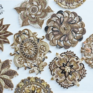 Può includere: Un assortimento di applicazioni decorative ricamate con perline in vari disegni floreali e geometrici. Le applicazioni presentano sfumature di oro, marrone e crema, con intricati ricami e abbellimenti. Il logo BohoTree.com è visibile in alto a sinistra.