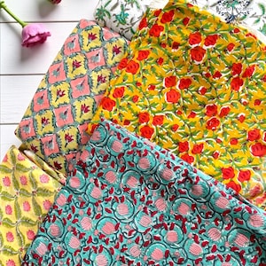 May include: A collection of colorful floral fabric samples. The fabrics feature various patterns, including red roses on yellow, pink and yellow geometric designs, and teal with pink floral motifs. The image is taken from a high angle, showcasing the vibrant textiles.