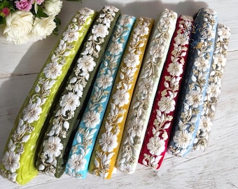 May include: Assortment of seven embroidered trim ribbons in various colors, including green, blue, yellow, white, red, and gray. Each ribbon features a white floral design with gold accents.