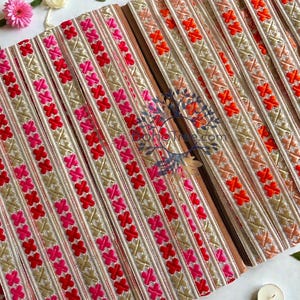 May include: Close-up of decorative trim with a repeating cross pattern. The trim features a gold background with red, pink, and orange embroidered crosses. The trim is likely used for embellishing clothing or craft projects.