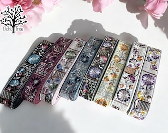 May include: Six different embroidered trim ribbons with floral and geometric patterns in shades of purple, blue, green, and beige. The ribbons are arranged in a row, with the purple ribbon at the top and the beige ribbon at the bottom.