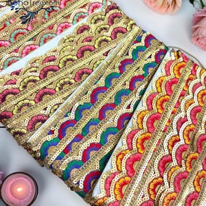 May include: Several rolls of decorative fabric trim featuring a scalloped edge with gold sequins and vibrant embroidery in pink, yellow, green, and blue. The trim displays the text BohoTree.com and is arranged in a layered, diagonal pattern.