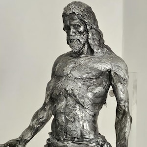 May include: A detailed, metallic sculpture of a man with long hair and a beard, arms outstretched. The figure is draped with cloth around the waist. The sculpture has a textured surface and is set against a plain background.