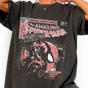 Puede incluir: Camiseta gris oscuro con un dise&ntilde;o de portada de c&oacute;mic vintage. El gr&aacute;fico incluye las palabras "Amazing Spider-Man" en rosa y blanco, detalles de c&oacute;mic y una ilustraci&oacute;n de Spider-Man. La camiseta tiene mangas cortas.