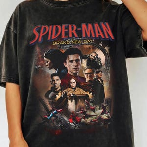Op de afbeelding: Donkergrijs T-shirt met een Spider-Man-afbeelding en de tekst "SPIDER-MAN BRAND NEW DAY". De afbeelding bevat afbeeldingen van personages uit de film. Het shirt heeft een vintage, versleten uitstraling.
