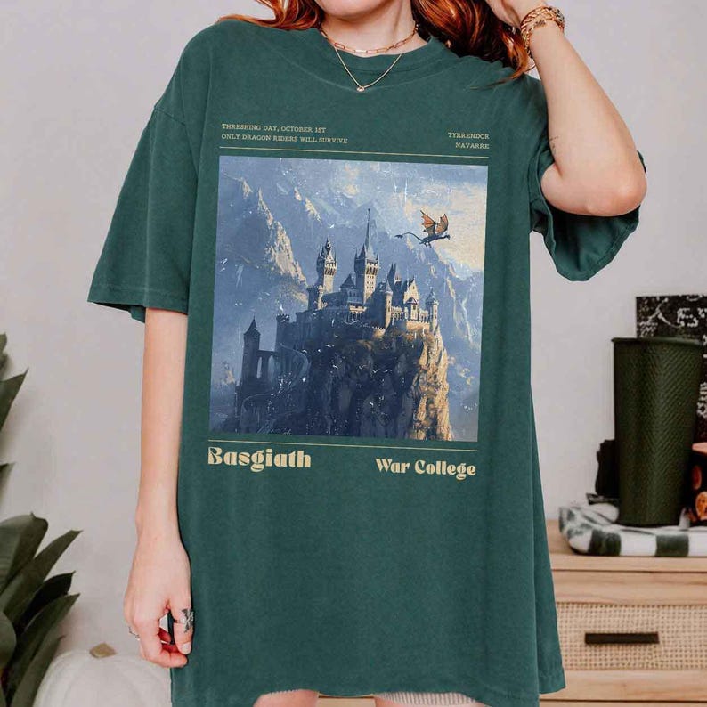 May include: Dark green t-shirt featuring a fantasy castle illustration with a flying dragon and the text "Basgiath War College". The shirt also includes the text "Threshing Day, October 1st, Only Dragon Riders Will Survive" and "Tiarendor Mavarre".