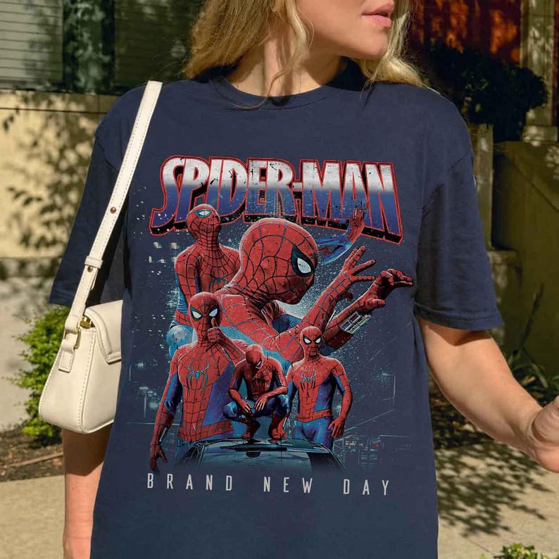 May include: Navy blue t-shirt with a Spider-Man graphic. The design includes multiple Spider-Man figures in red and blue, with the text "SPIDER-MAN" and "BRAND NEW DAY". The graphic is a collage of Spider-Man poses.